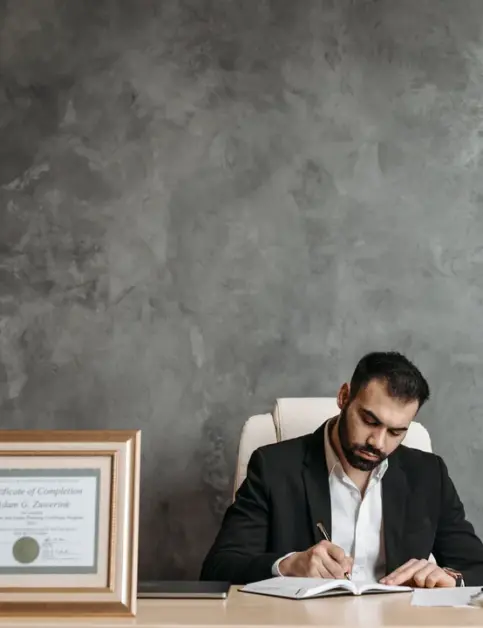 Lawyer writing at a desk beside a framed certificate and a lady justice statue