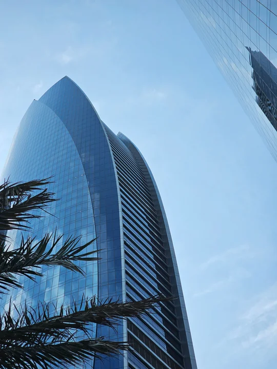 Modern glass skyscraper against a blue sky with palm trees