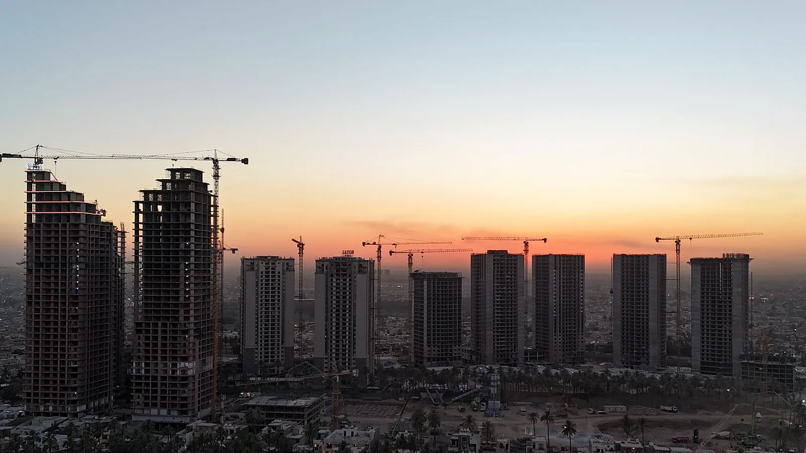 Baghdad skyline at sunset with high-rise towers and construction cranes, reflecting foreign investment and development in Iraq