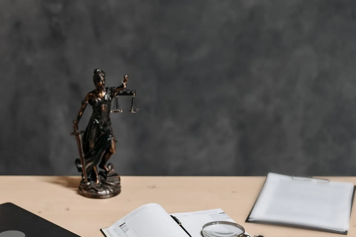 Lady Justice statue on a lawyer’s desk with documents and a magnifying glass, representing legal review of foreign ownership and investment in Iraq